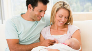 A couple sitting on a sofa with a newborn baby and smiling